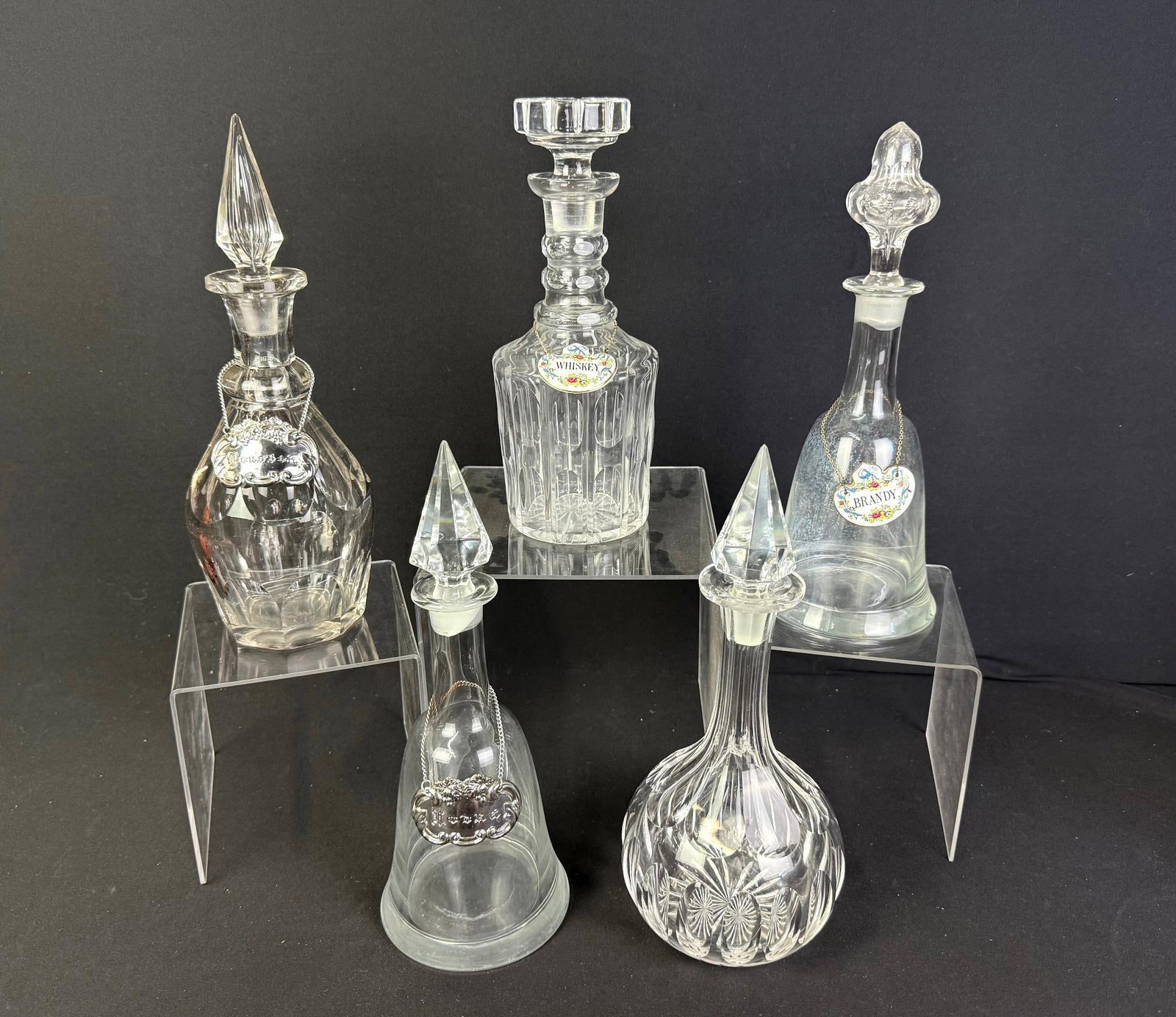 5 Glass Decanters: Four include liquor tags. 5" to 5-1/2" wide x 10" to 12-1/4" high. 