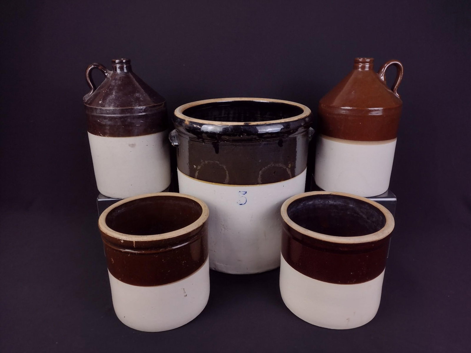 3 Stoneware Crocks & 2 Jugs: Largest 5 gallon crock measures 12" x 12" x 13-1/4. Smallest measures 7-1/2" x 7-1/2" x 7-1/2". Some chipping of paint and on bottom.