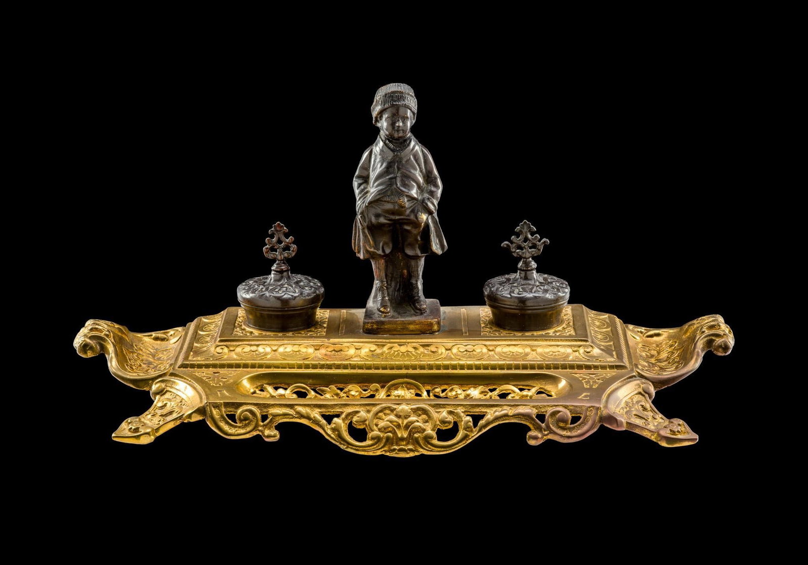 Maitland-Smith Brass Double Inkwell Desk Set: Central bronze sculpture of a young boy standing between two lidded inkwells. Ornate openwork gilt bronze base. Some rubbing. Measures 9-1/2" height x ~20" long. 