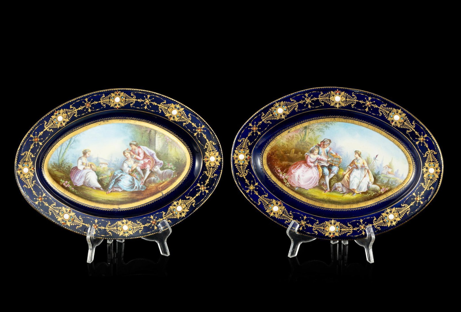 Pair of Russian Imperial Porcelain Cabinet Platters: Each featuring a cobalt rim with raised gilt scrolling and enamel accents. Hand painted French pastoral courting scenery to center. Blue factory mark of a stylized crown over a ribbon banner enclosing