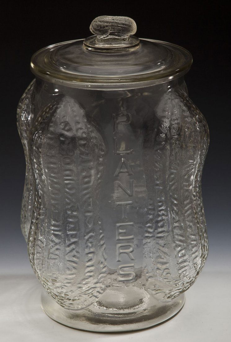 Large Planters Peanut Jar with 4 Peanut Sides: DESCRIPTION: Large Planters Peanut jar with four corners in the form of peanuts. Between each of the peanuts reads "Planters". Lid with peanut as a handle. MEASUREMENTS: 8-1/4" x 8-1/4" x 14" high wit