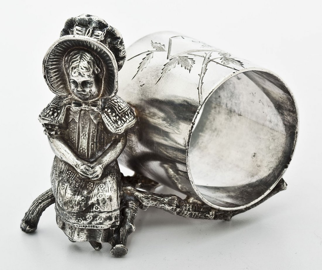 Victorian Kate Greenaway Napkin Ring: DESCRIPTION: Victorian Kate Greenaway silver plate figural napkin ring with girl in a bonnet seated on a branch. The ring itself has hammered detailing with a floral motif framing a windmill in a coun