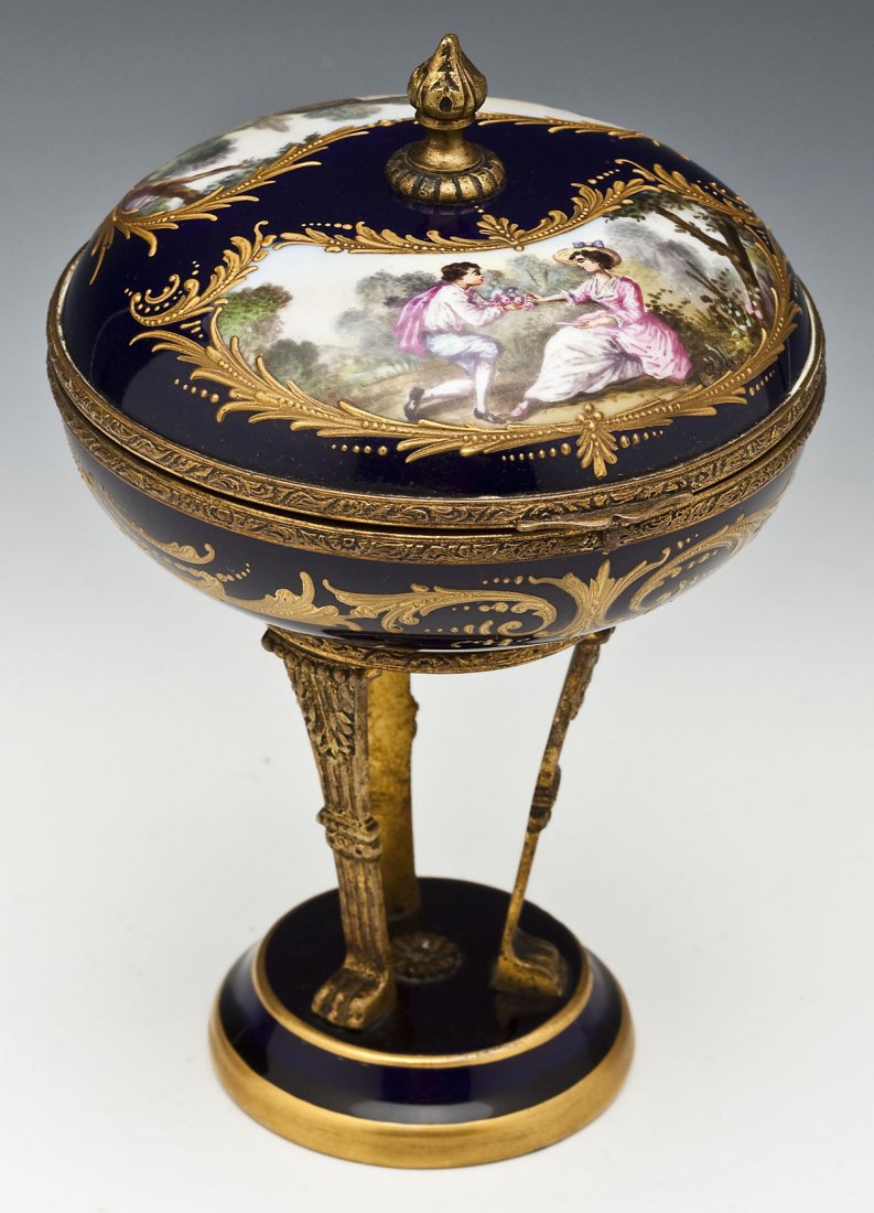 Sevres Porcelain Box on Stand: DESCRIPTION: Sevres porcelain box on stand with ormolu mounts. Round box with hand painted cartouches of a couple and landscape to lid and resting on three curved legs ending in paw feet on a round ba