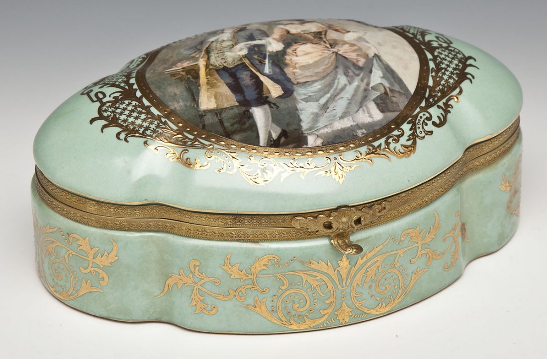 Sevres Porcelain Dresser Box: DESCRIPTION: Sevres porcelain dresser box with ormolu mounts. Lid with transfer decorated cartouche depicting a courting couple, bordered by gilded painting with a leaf and scroll motif. The same moti