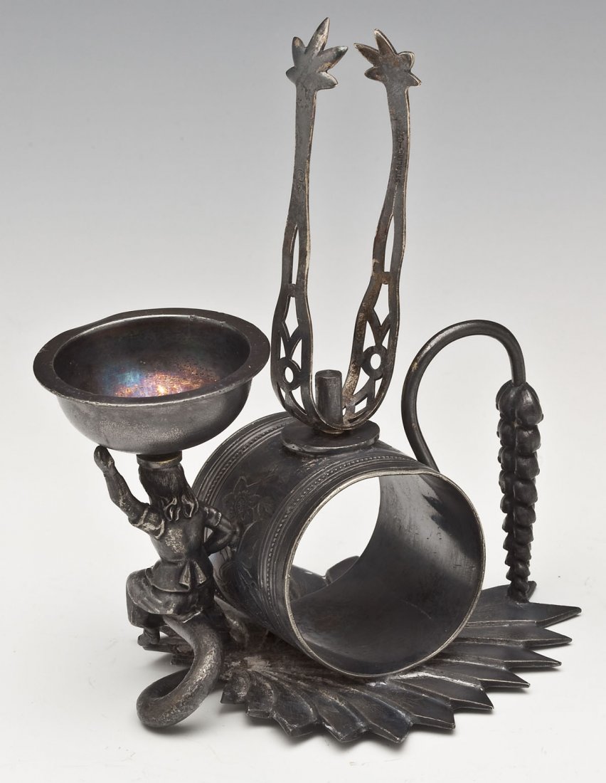Meriden Silver Plate Co. Figural Napkin Ring: DESCRIPTION: Meriden Silver Plate Co. figural napkin ring. Quadruple plated. Attached tongs, with small bowl held up by a figure, all positioned on a leaf base. Makers mark on bottom and "111". MEASUR