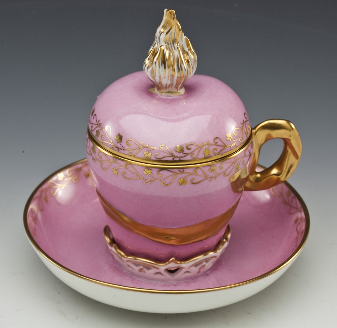 KPM Porcelain Covered Cup and Saucer: DESCRIPTION: KPM porcelain covered cup and saucer. Pink and white with gold painted detailing, and gold painted handle of lid and cup. Marked for KPM under cup and saucer. MEASUREMENTS: Cup with lid 5
