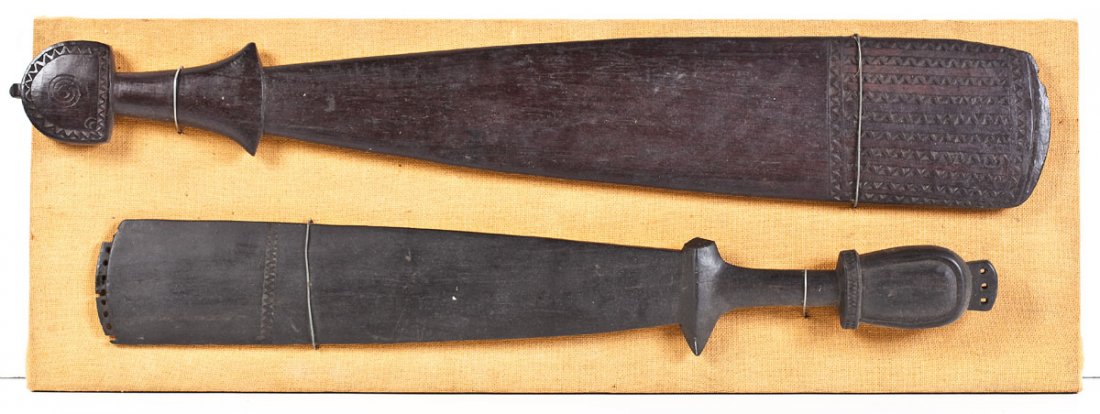 2 Massim Tribe Carved Wood Clubs Papua New Guinea: DESCRIPTION: Two Massim Tribe carved wood clubs, Trobriand Islands, Papua New Guinea. Paddle form with carved designs at tops and to handles. Late 19th/early 20th century. Attached to fabric covered b