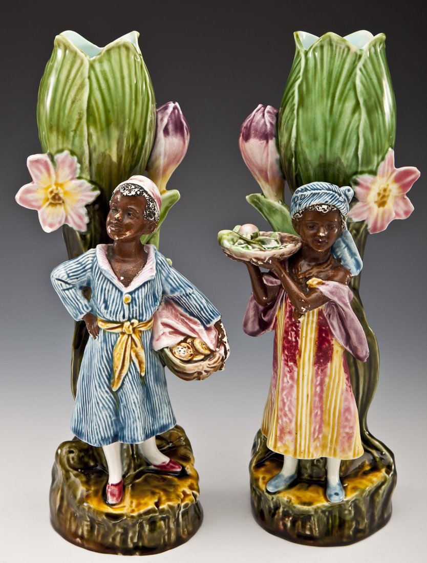 Pair of Majolica Figural Black Americana Vases: DESCRIPTION: A pair of Majolica figural vases in the form of African children holding trays of food in front of floral and leaf vases on naturalistic bases. Each with impressed number markings under b