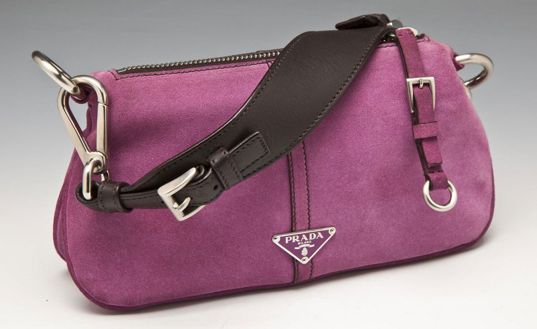 Prada Purple Suede Handbag: DESCRIPTION: Purple suede hangbag by Prada. Brown leather strap attached at either end with carabiner clips that can be removed to create a clutch purse. Zippered enclosure, black lining and zippered