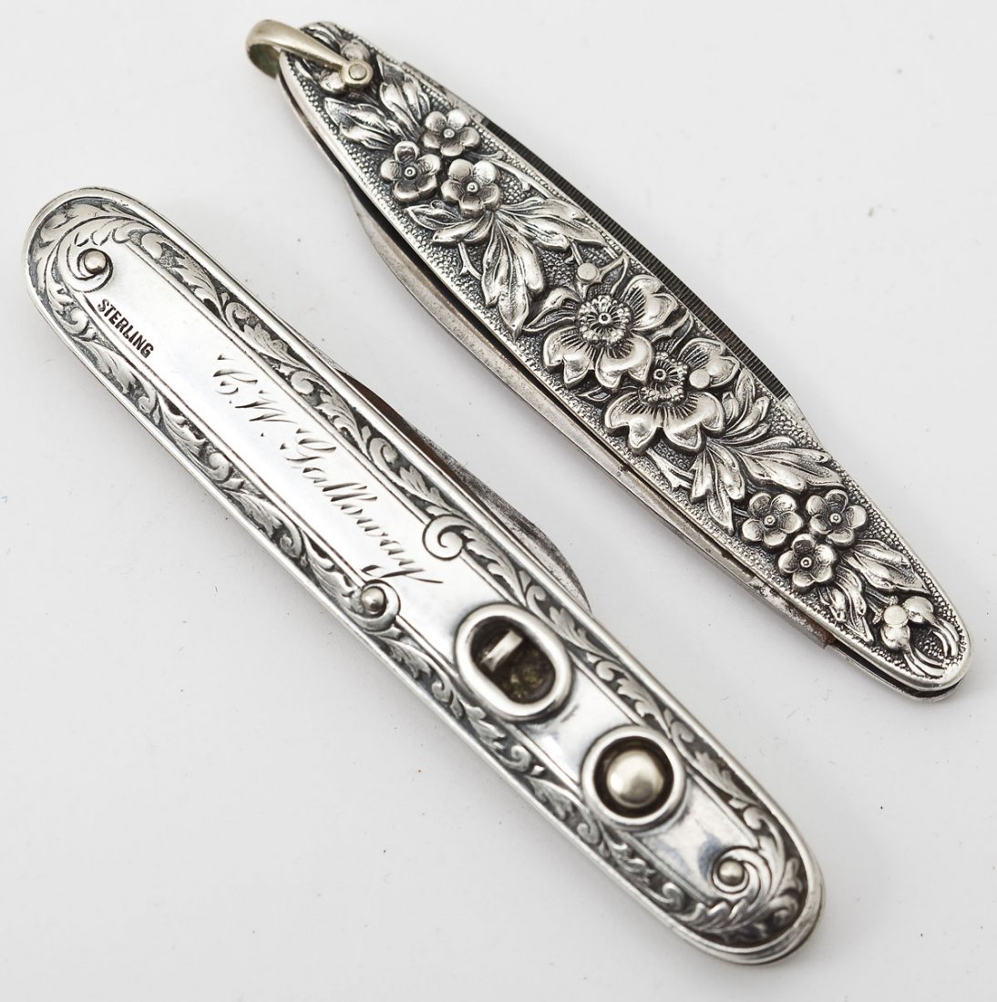 2 Sterling Pocket Knives: DESCRIPTION: Two sterling pocket knives. Includes: 1) Floral decorated with two blades, marked for Ulster Knife Co. 3-1/8" long. 2) Scroll decorated with two blades with push button mechanisms with lo