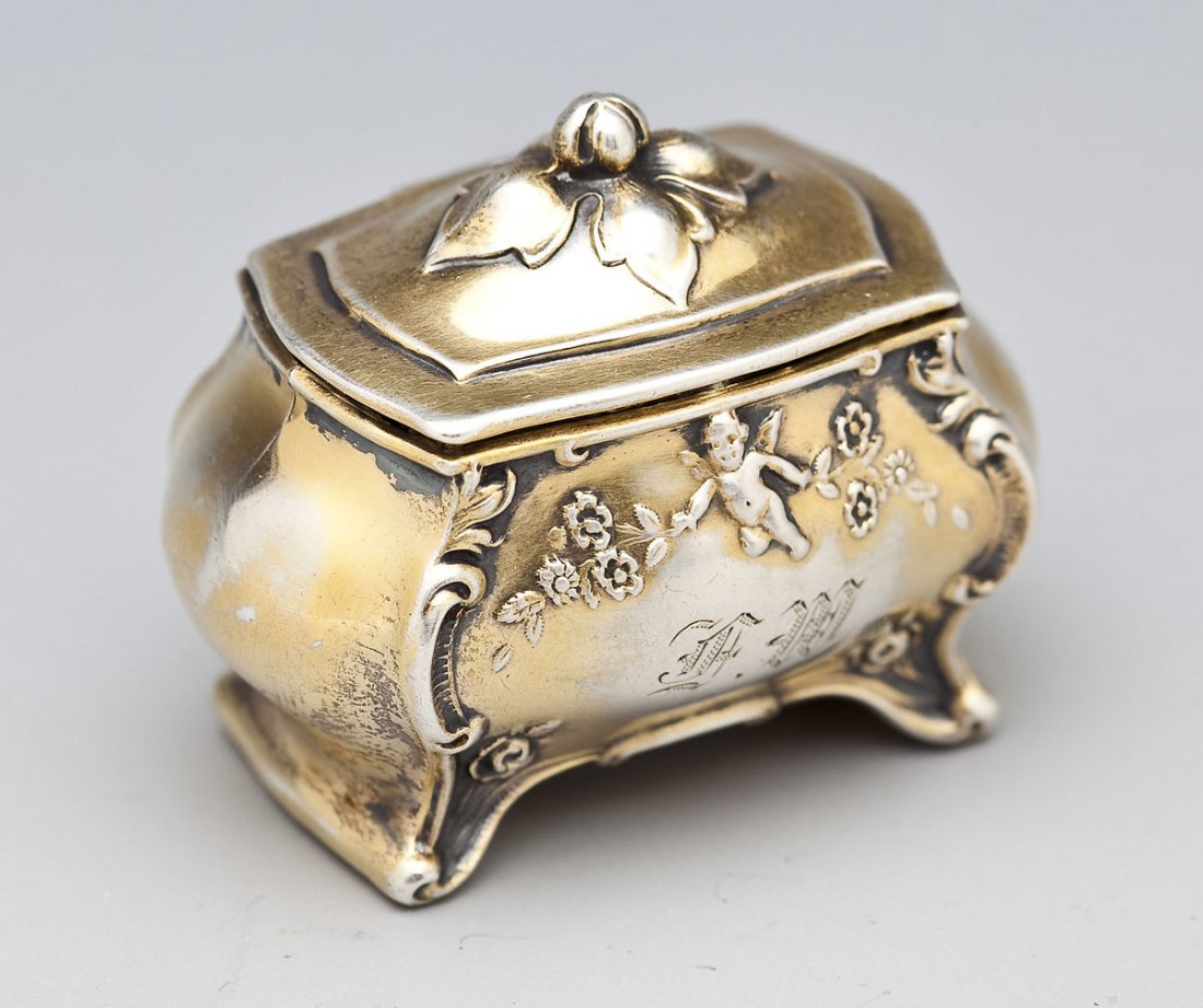 Simons Bros. Sterling Silver Ring Holder: DESCRIPTION: Sterling silver ring holder with gilt wash in the form of a bombe style chest decorated with scrolling, flowers and putti. Front monogrammed "FM". Marked to inside rim "Sterling 1939" wit