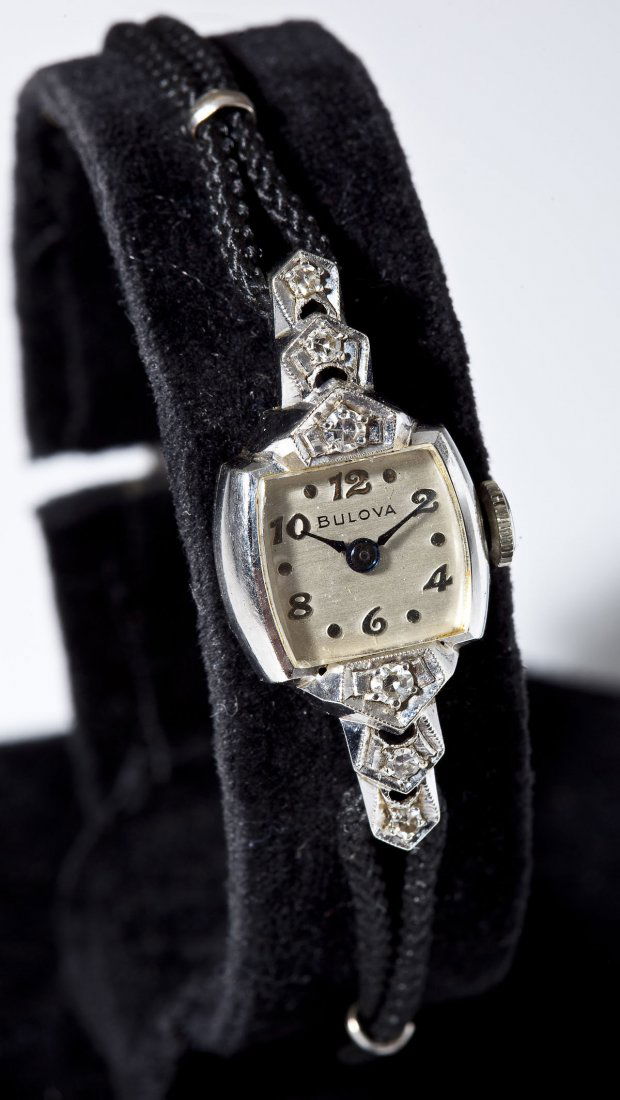 Lady's Bulova 14K & Diamond Wristwatch: DESCRIPTION: Lady's Bulova wristwatch on black cord bracelet. Silvered dial with silver numerals, marked "Bulova". Marked 14K white gold case set with six small diamonds. Approximately .32 ctw. Moveme