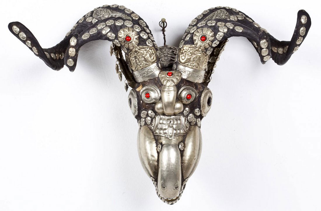 Tibetan Silver Mounted Ram Skull with Coral: DESCRIPTION: A Tibetan silver mounted ram skull decorated with tiny skulls and inset with coral cabochons. MEASUREMENTS: 16-1/2" wide x 8-1/2" high. CONDITION: Some wear and patina as expected with ag