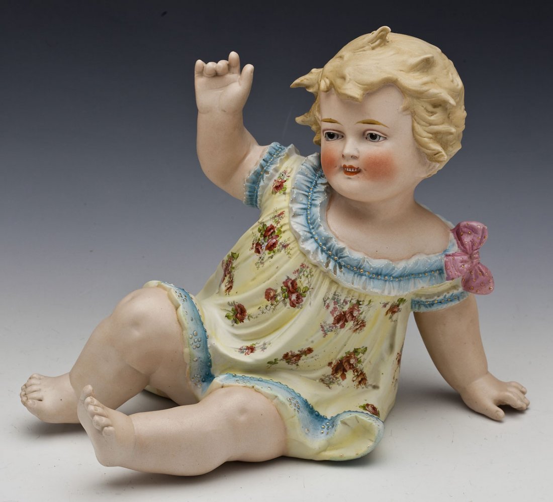 German Conta & Boehme Bisque Piano Baby: DESCRIPTION: A German bisque piano baby in flowered smock with gilt decoration. Marked "Germany" with Conta & Boehme shield mark. MEASUREMENTS: 11-1/2" long x 10" high. CONDITION: Minor wear as expect