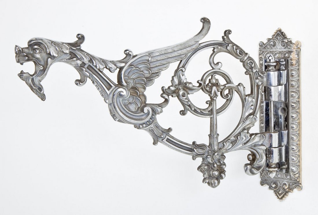Cast Metal Swinging Wall Bracket: DESCRIPTION: Cast metal swinging wall bracket. With flourishes, dragon face and wings, and floral motifs. With hardware. MEASUREMENTS: 15" long x 10" tall x 2-3/4" wide. CONDITION: Minor scratches, pa