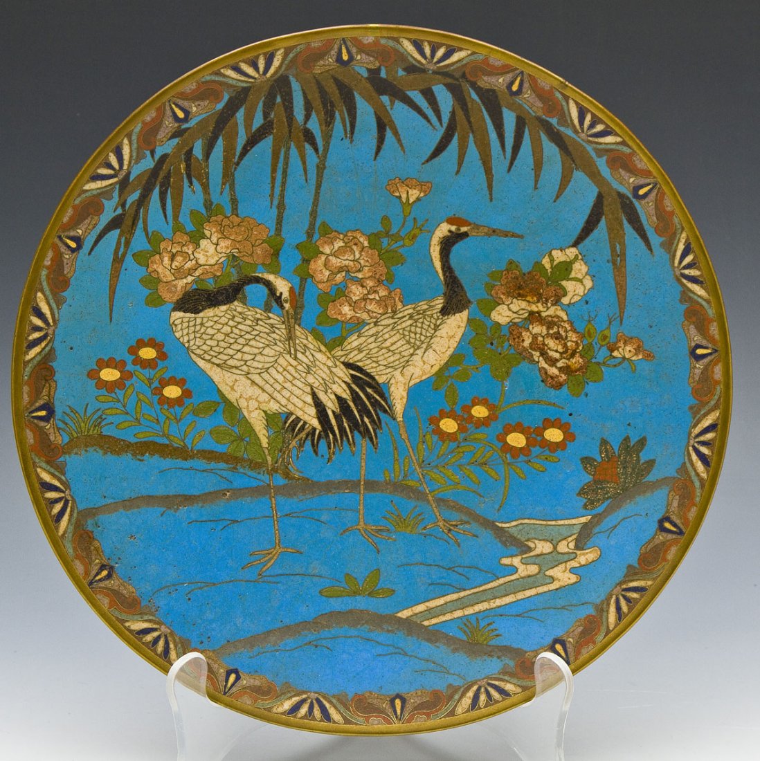 Japanese Cloisonne Charger with Cranes: DESCRIPTION: Japanese cloisonne charger decorated with cranes amongst foliage. Brass rim. Japanese old paper label on reverse, secured with tape. MEASUREMENTS: 11-7/8" diameter. CONDITION: Minor craqu