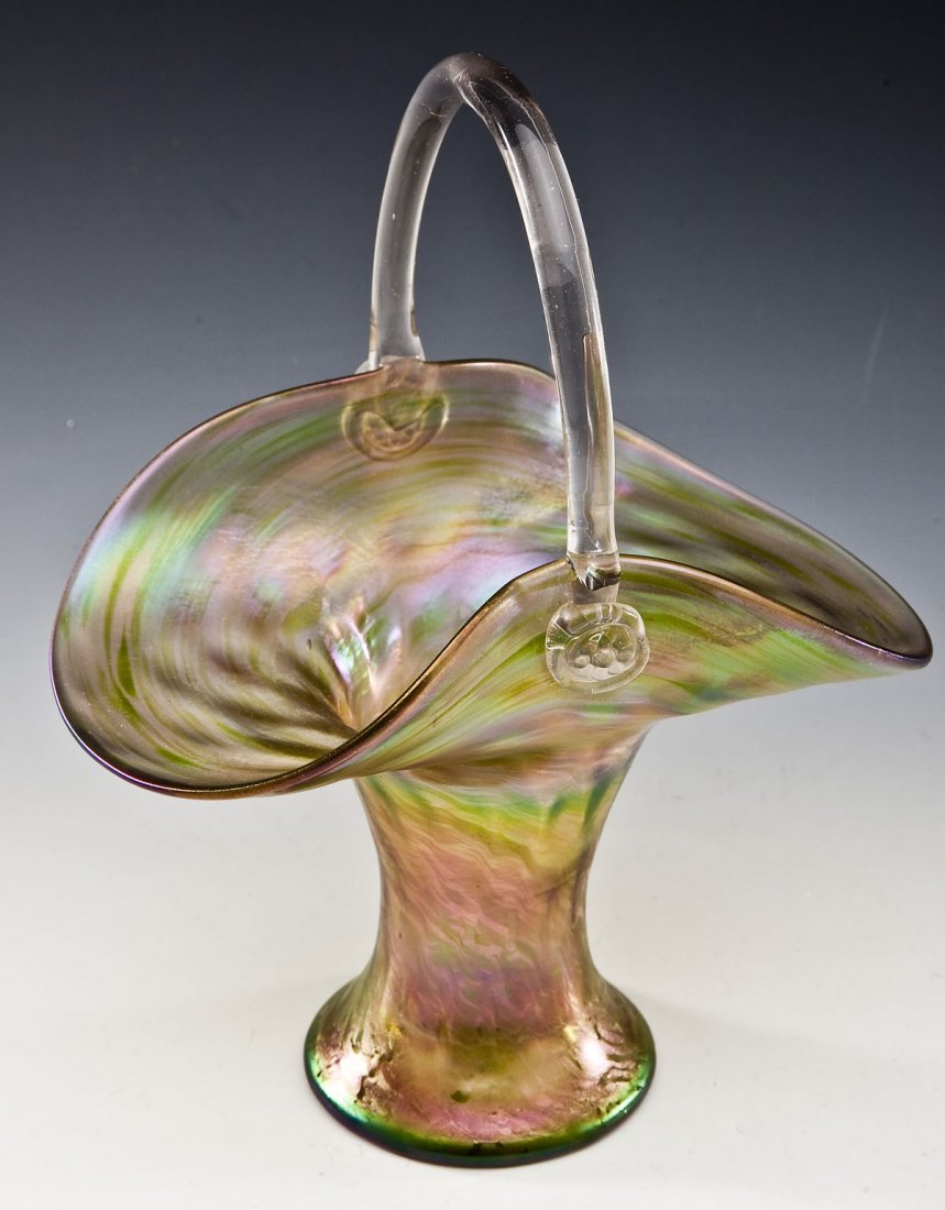 Loetz Type Iridescent Green Glass Basket: DESCRIPTION: Loetz type iridescent green glass basket with clear glass handle. MEASUREMENTS: 10-1/4" tall x 8-1/8" at widest point. CONDITION: Minor chip to handle near lip of basket.