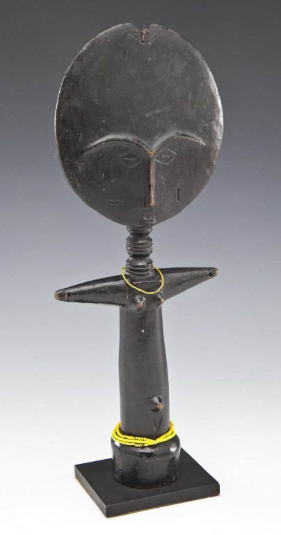 Ashanti Akuaba Fertility Figure: DESCRIPTION: Ashanti Akuaba fertility figure. Disc-shaped head, black lacquered surface, pole-shaped body, with yellow beads and cording. On stand. PROVENANCE: From the Saul and Florence Putterman Col