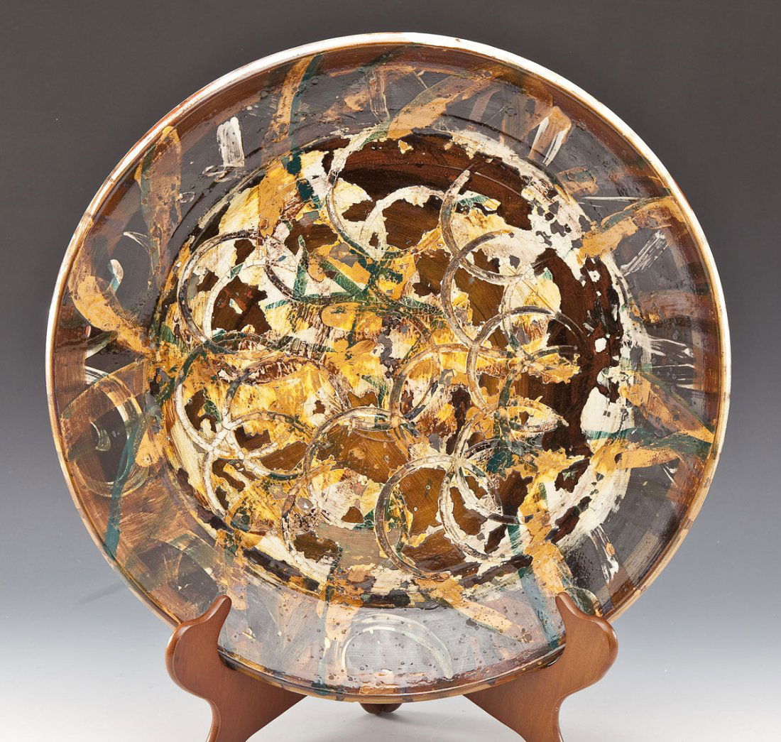 Florence Putterman (American, B. 1927): DESCRIPTION: Florence Putterman (American, B. 1927). Wheel-thrown shallow bowl with multi-colored glaze. with incised circular pattern to surface. Wood panel and wire hook attached to base for hanging