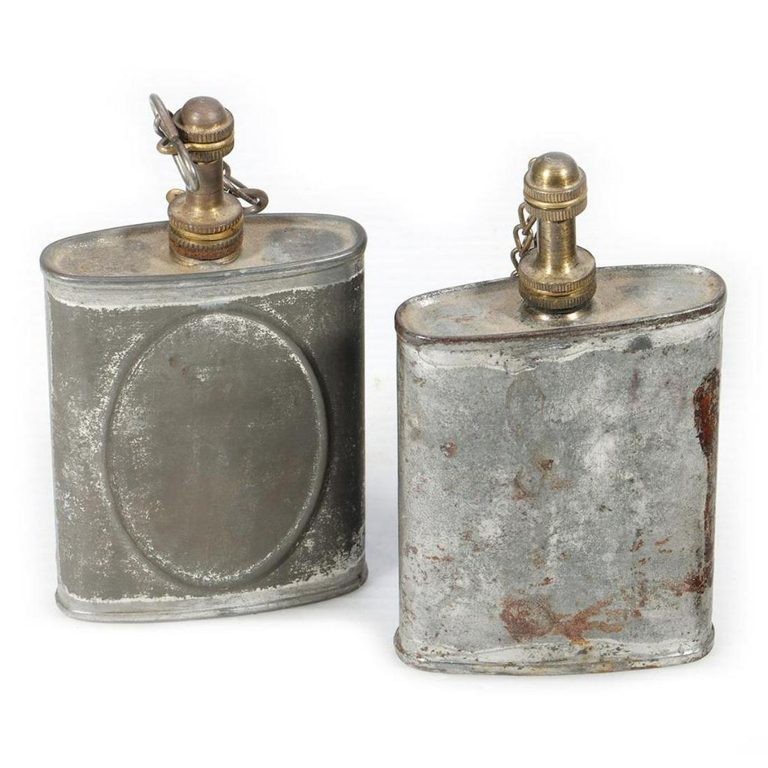 Two galvanized antique hip flasks.: 1. Galvanized antique hip flask. Brass top fittings. Sides have embossed ovals but no labels. No branding. Dirt but no rust. Shiny on bottom but the rest of the surfaces are dull. 2. Galvanized antiqu