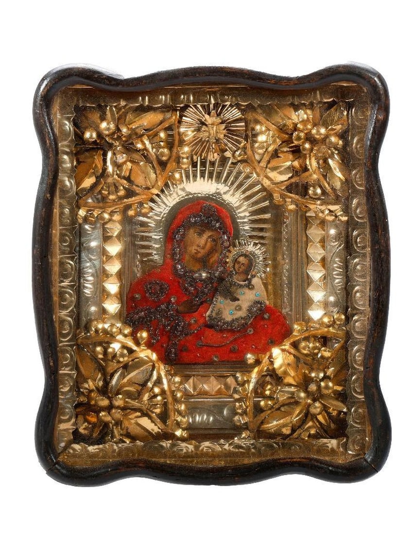 An Icon of the Theotokos, in Kiot.: Eastern Europe, 19th/20th Century. A painted icon of the Theotokos, Mother of God, with gilt-embroidered and beaded red and white cloth garments and ornate foil liner, in a scalloped shadowbox frame/k