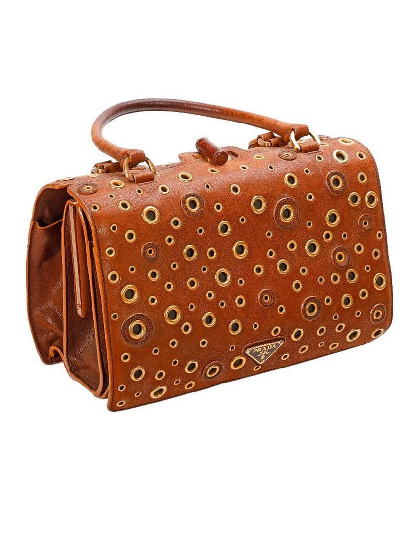 Prada Suede Grommet Handbag: A Prada, Milano brown suede handbag with gold-toned grommets, toggle closure, and central compartment. Metal Prada labels on outside and interior. 11" x 6 3/4" x 5 1/2". Condition: overall good, light