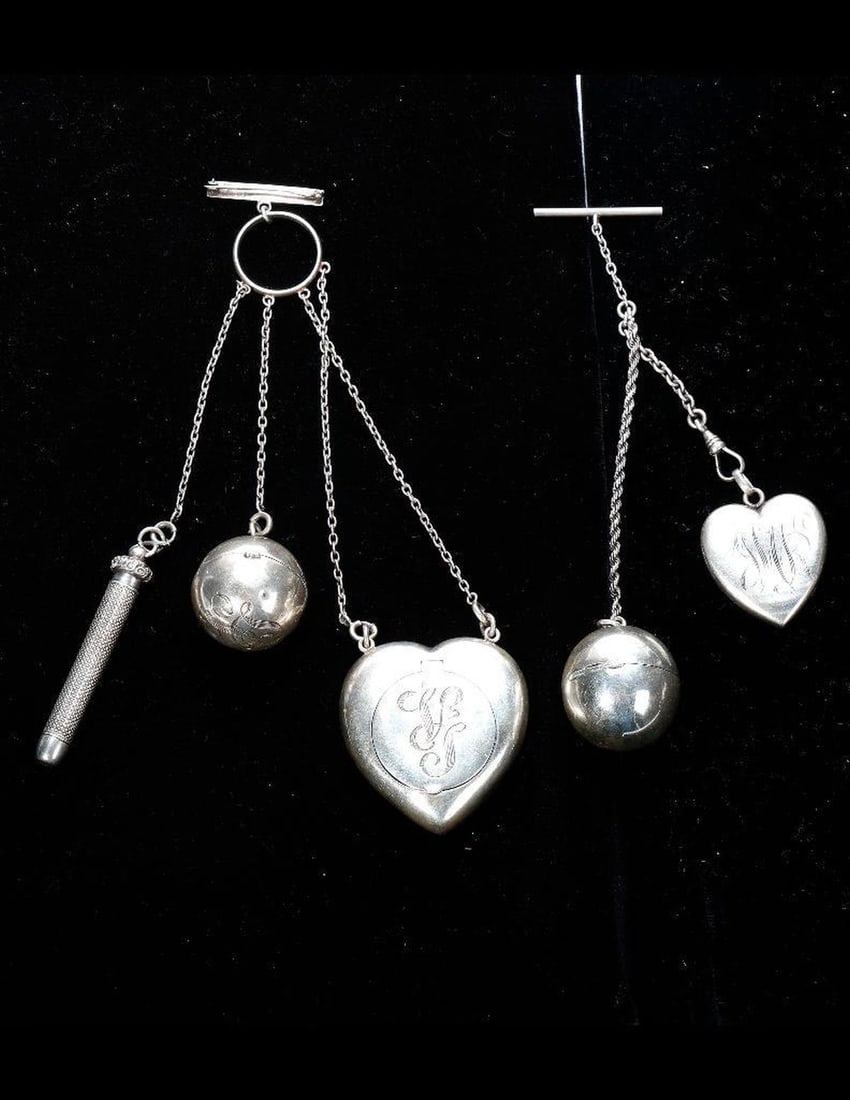 Two silver chatelaines: one with brooch attachment, suspending a heart-shaped box, a ball form coin holder and a retractable pencil; the other with toggle top, suspending a heart-shape locket and ball form coin holder; gross