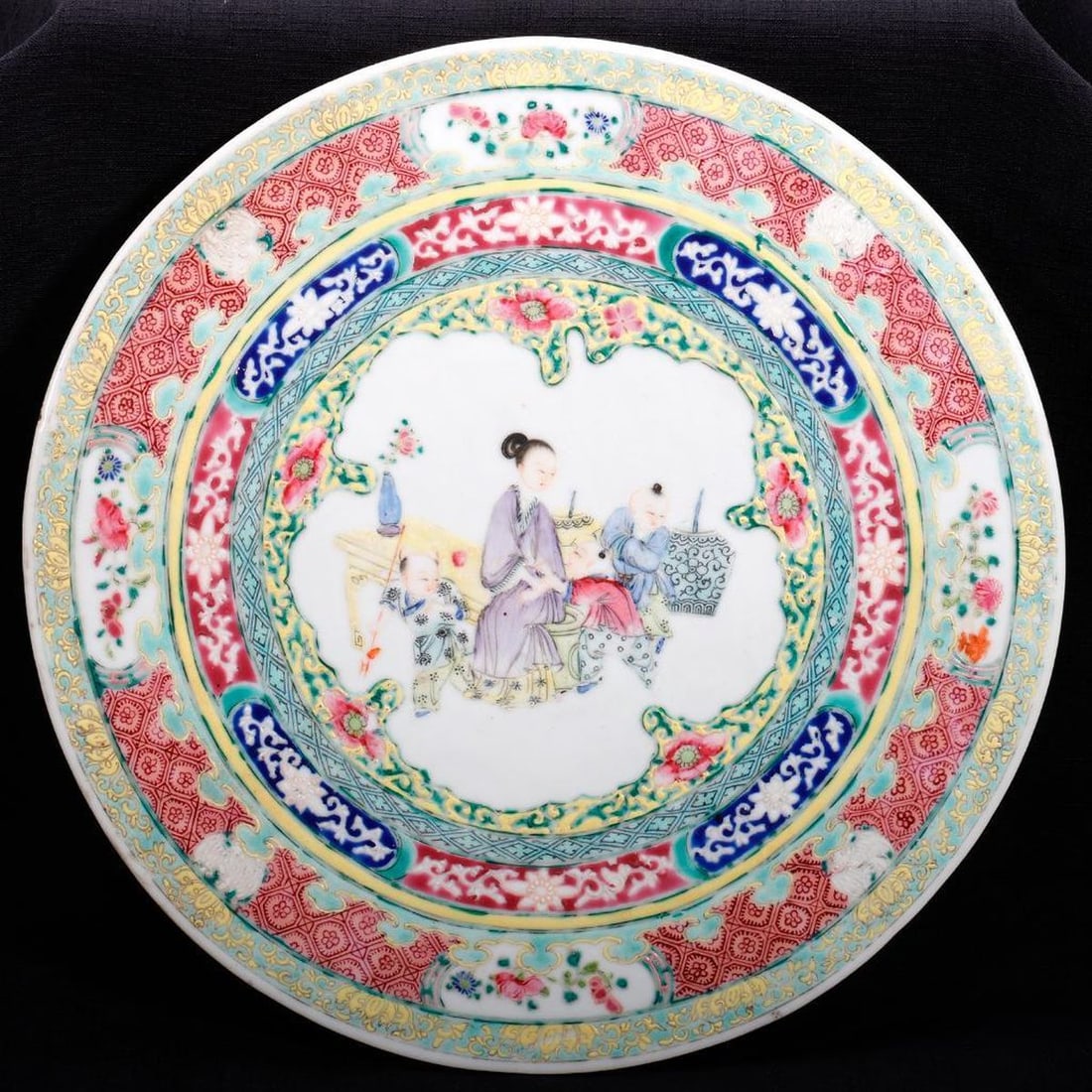 Chinese Famille Rose Porcelain Plaque: Qing Dynasty, of disc form with a lady playing with children, painted in purple, blue, yellow and rose, enclosing multiple blossom, lattice and lotus bands, 11.25"d. Condition: some wear to enamel wor