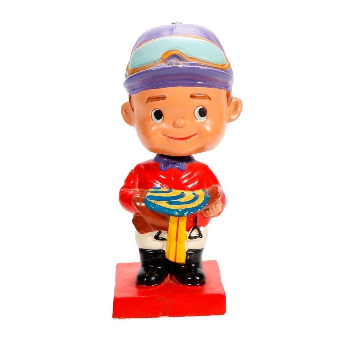 1962 Jockey Nodder/Bobble Head: The composite nodder figure of a jockey in red and purple, holding a saddle; the base stamped copyright 1962, Japan. 6 1/4" tall. Condition: overall good; a few small spots of paint loss.