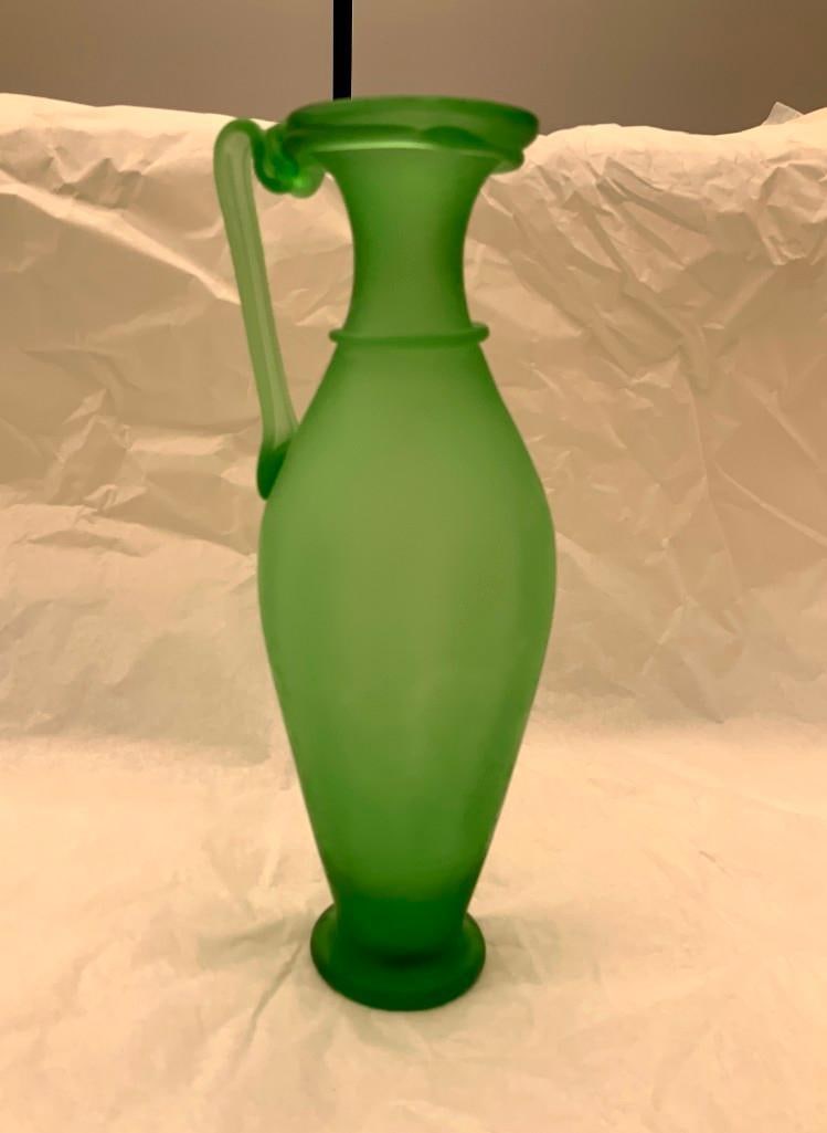 CCAA GLASGALERIE KOLN Glass Jug With Handle: Reproduction of antique glass, pitcher shaped, one handle, frosted green glass. 11 x 4 x 3 3/4 inches (27.9 x 10.2 x 9.5 cm) Provenance: CCAA Glass Gallery Cologne These replicas, based on Roman origi