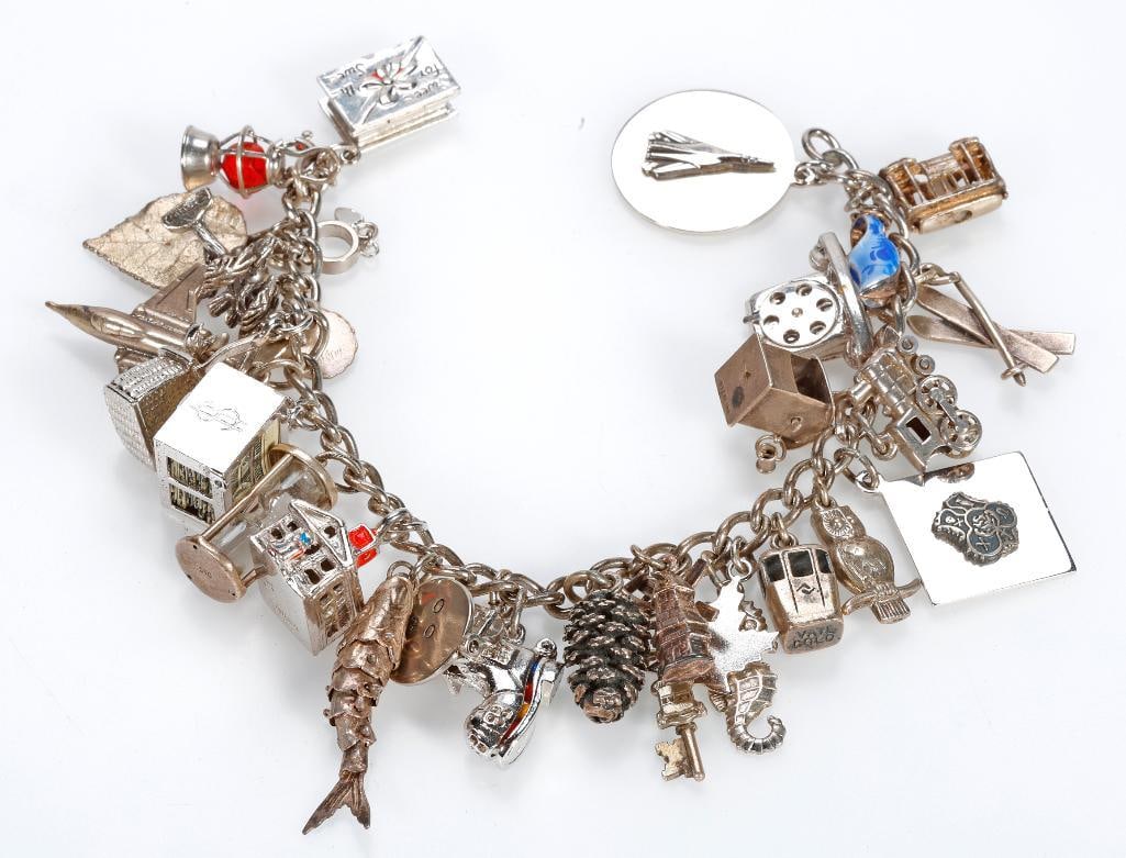 A silver and metal charm bracelet: suspending 27 charms including rotary phone, cable car, enamel clogs, skis, box of chocolates, lantern, hourglass, the Concorde, an articulated well, windmill, and old lady-in-the-shoe, dollar bill ba