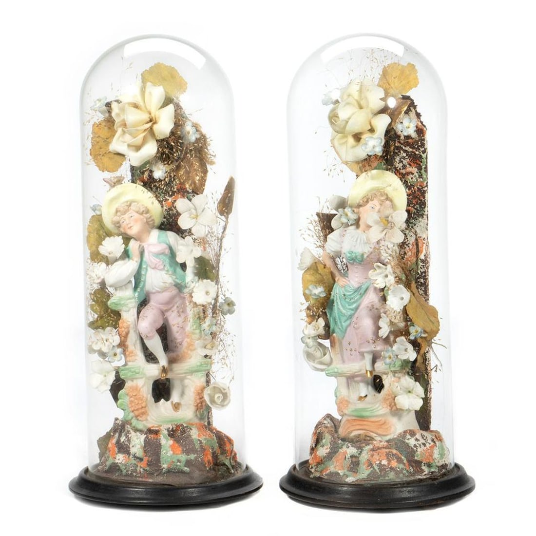 Pair Victorian Floral and Figural Domes: Each with ceramic work floral garlands surrounding porcelain figures of a young lady and gent under glass domes. 15 1/4in. h. 5in. d. Condition: Very good.