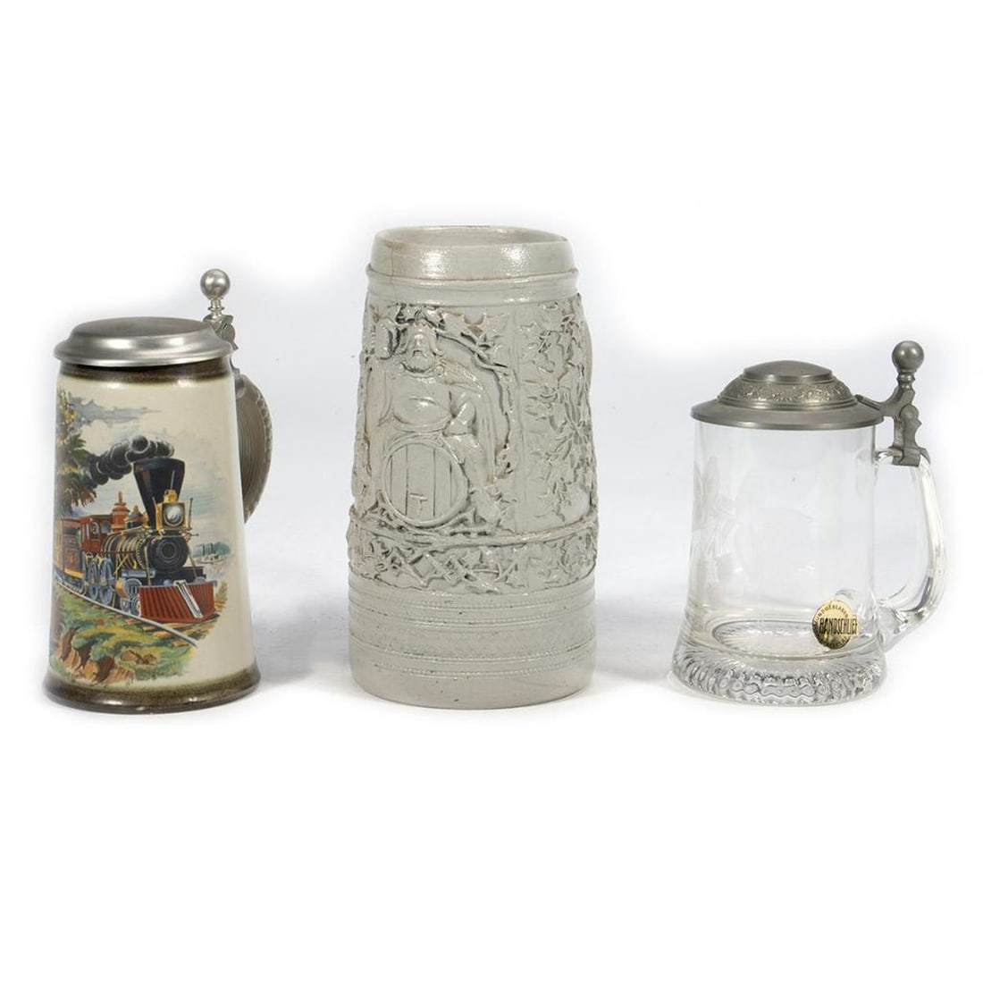 Collection of Three German Steins: One of gray-glazed earthenware; one with a train design and pewter lid; the third is Handschliff Crystal with etched decoration and a pewter lid. Heights 8in. 6 1/2in, 6in. Condition: Overall