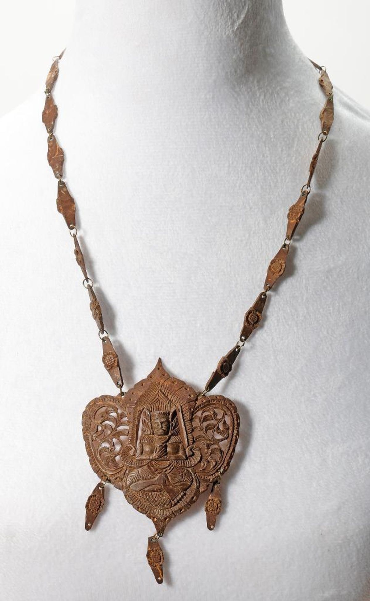 Two Ethnic Southeast Asian or Pacific Island Necklaces: Comprising a Southeast Asian coconut shell necklace with a central seated deity figure, length approx. 13"; the second, a Pacific Island necklace consisting of fringed raffia and nodular cowrie shell