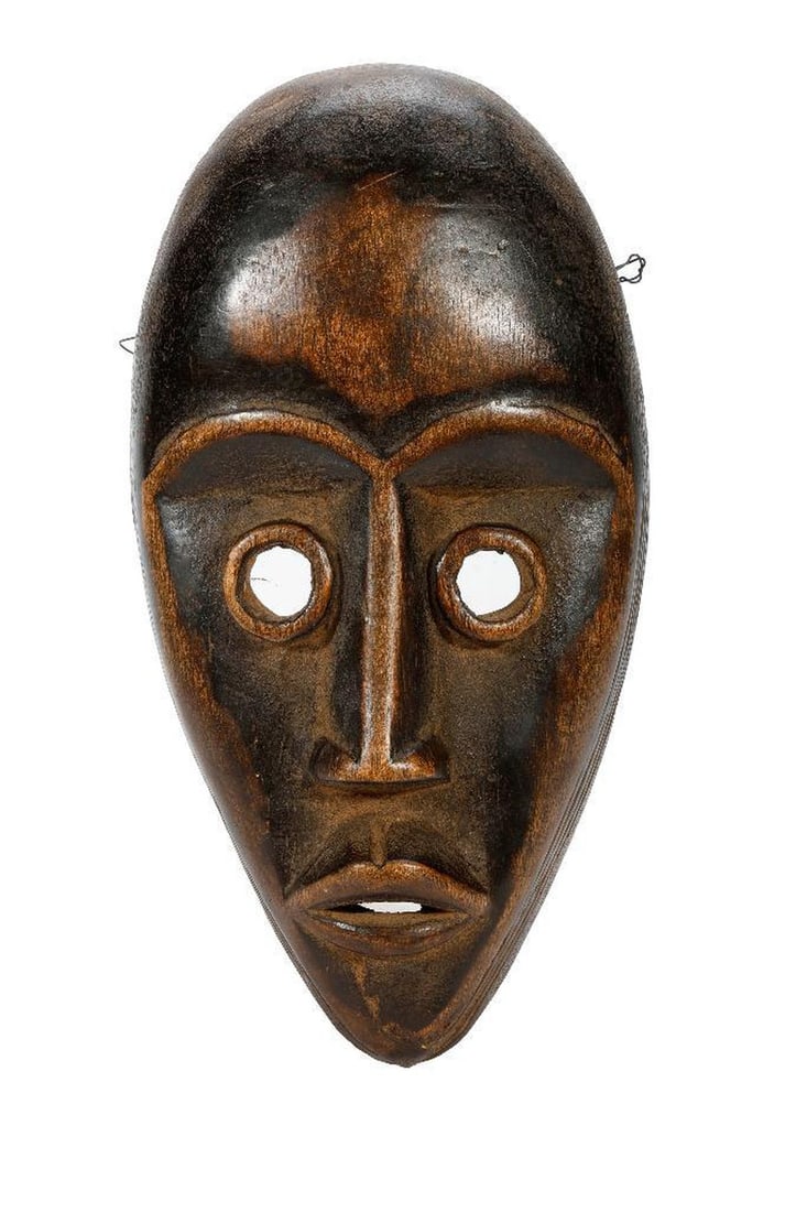 An African Ivory Coast Carved Mask: The elongated face with arched brows, round eyes, and multiple holes around the sides of the mask. 11 1/4" x 6". Condition: spots of wear/polish inside, and on the raised features of the face.