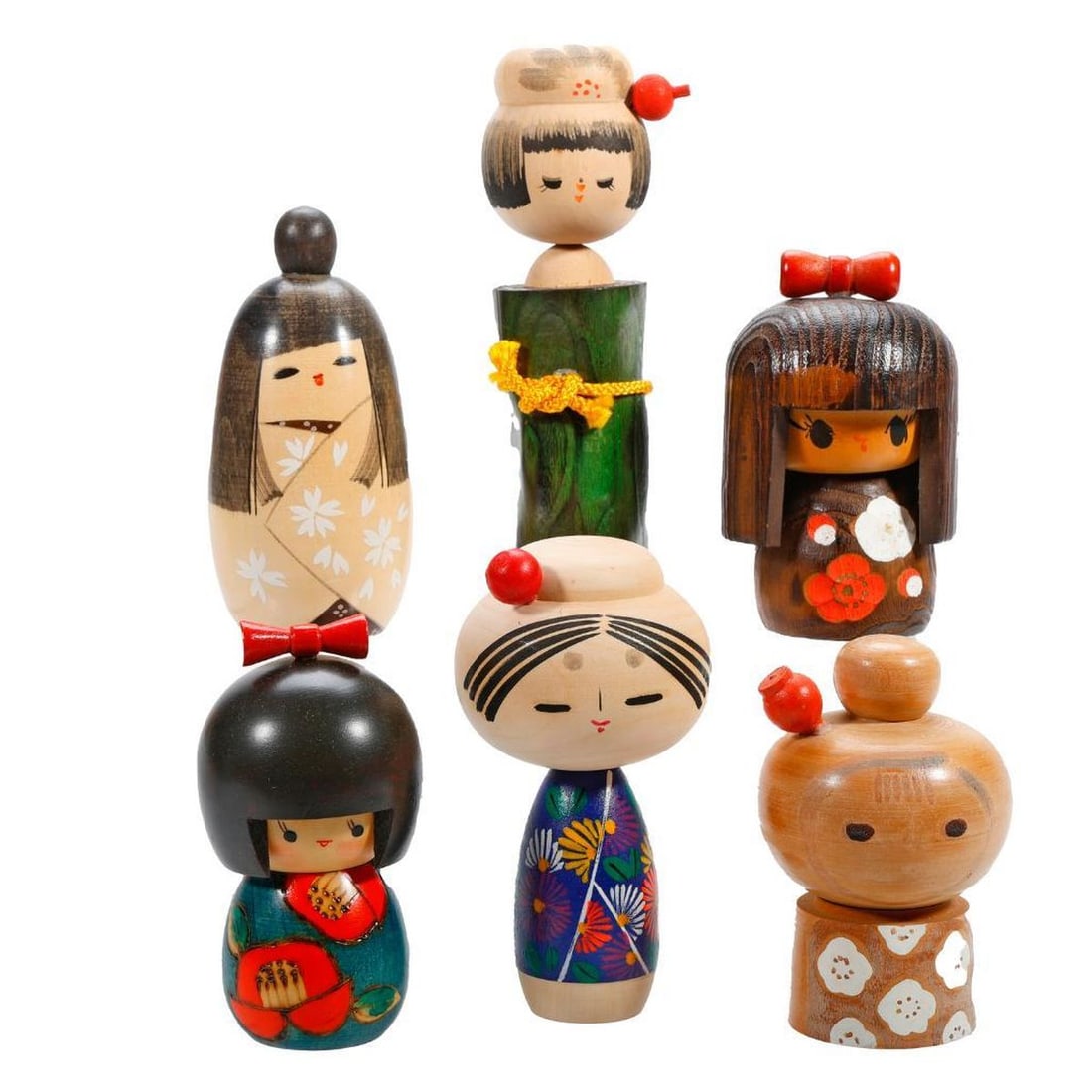 Six Japanese Kokeshi Girl Dolls: Comprising five dolls wearing a kimono painted with flowers, two having an applied "helmet" or bowl cut hair, a sixth doll with a body fashioned as green stained tree trunk tied with yellow rope, incl
