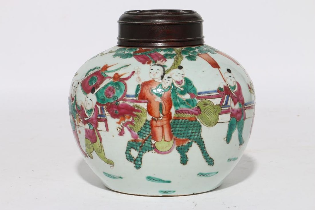 A Famille Rose Ginger Jar: The porcelain ginger jar with a scene of celebratory figures and fu dog in a garden; with a pierced carved wood lid. Height 8"; width 8". Condition good.