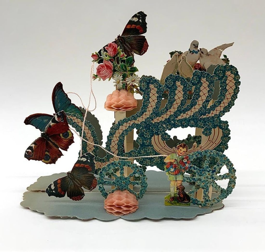 Vintage Oversized Pop-up Valentine, Carriage and Butterflies: A pop-up Valentine card with color illustration of flowers in shape of a carriage, young boy with small dog on front holding two bouquets of flowers with various butterflies and doves. Medium: paper,