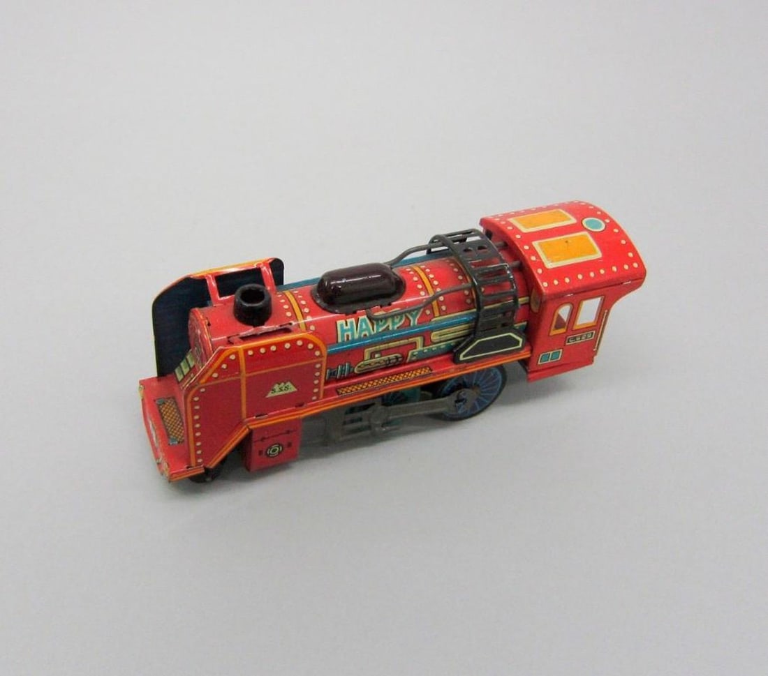 Sanesu Locomotive Train: The red tinplate toy locomotive with "Japan" printed on side. Dimensions: 2 1/4 x 6 x 1 1/2 inches (5.7 x 15.2 x 3.8 cm). Condition: Scattered paint loss and scratches throughout. Rust on exposed
