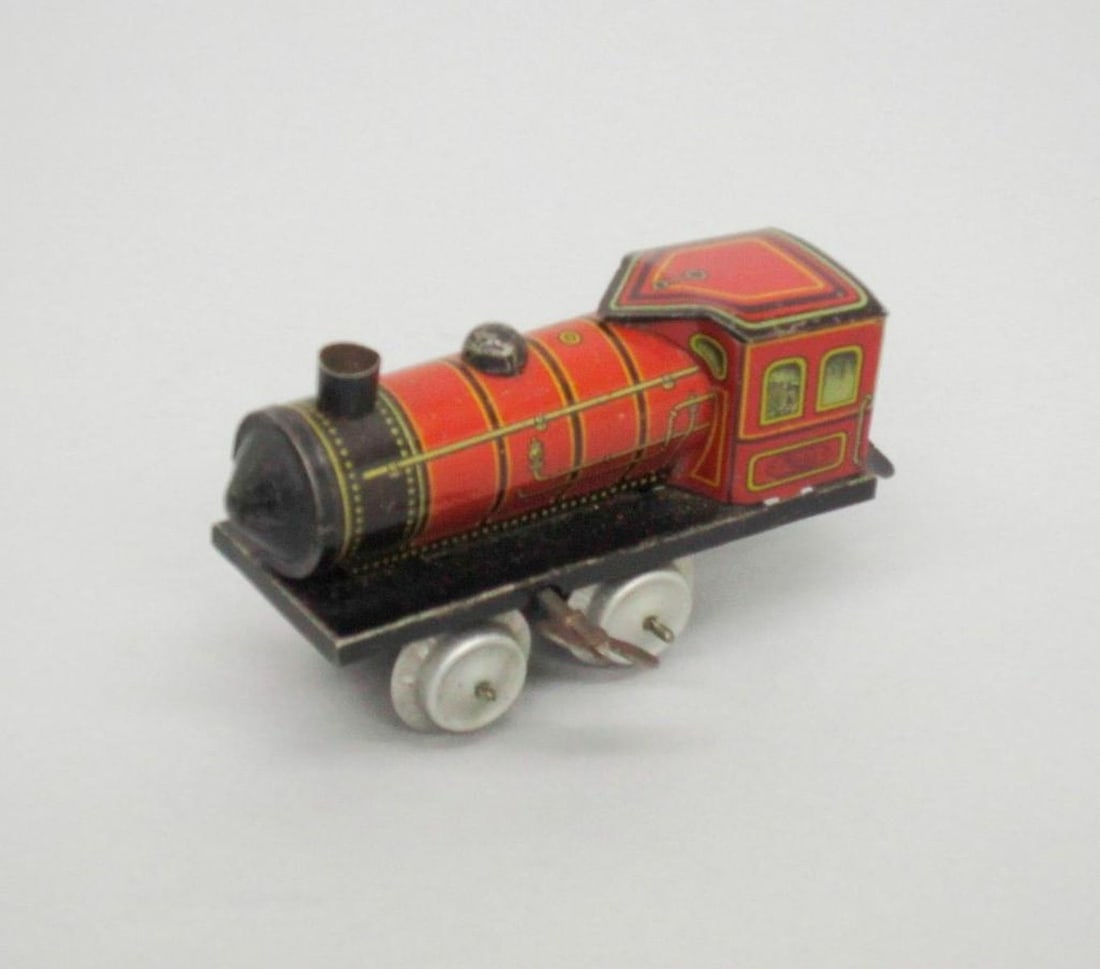 Huki Train Locomotive: Toy locomotive train; red exterior with black and gold details; wind-up key on side. Dimensions: 2 1/4 x 2 1/4 x 4 inches (5.7 x 5.7 x 10.2 cm). Condition: Scattered scratches throughout. Minor