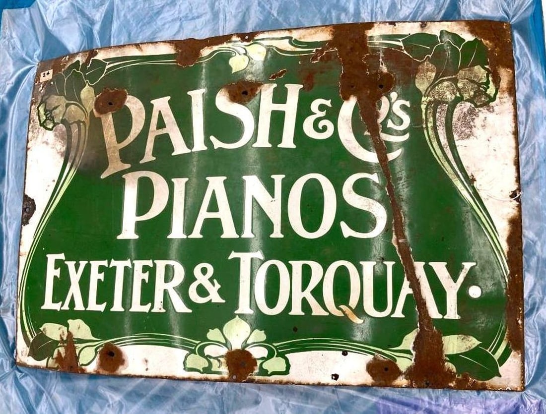 English Paish and Co. Pianos Advertising Enameled Sign: Circa 1920, the green enameled rectangular sign with white lettering reading PAISH & CO. EXETER & TORQUAY an a faux painted white ribbon tied banner to bottom folding upwards on left and right. Dimens