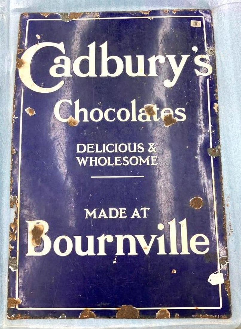 English Cadbury's Chocolates Enameled Sign: Circa 1930, the blue enameled metal rectangular sign reading "Cadbury's Chocolate/Delicious & Wholesale/Made at Bournville" Dimensions: 36" x 24" (91.4 x 61 cm) Overall fair condition, Some enamel los