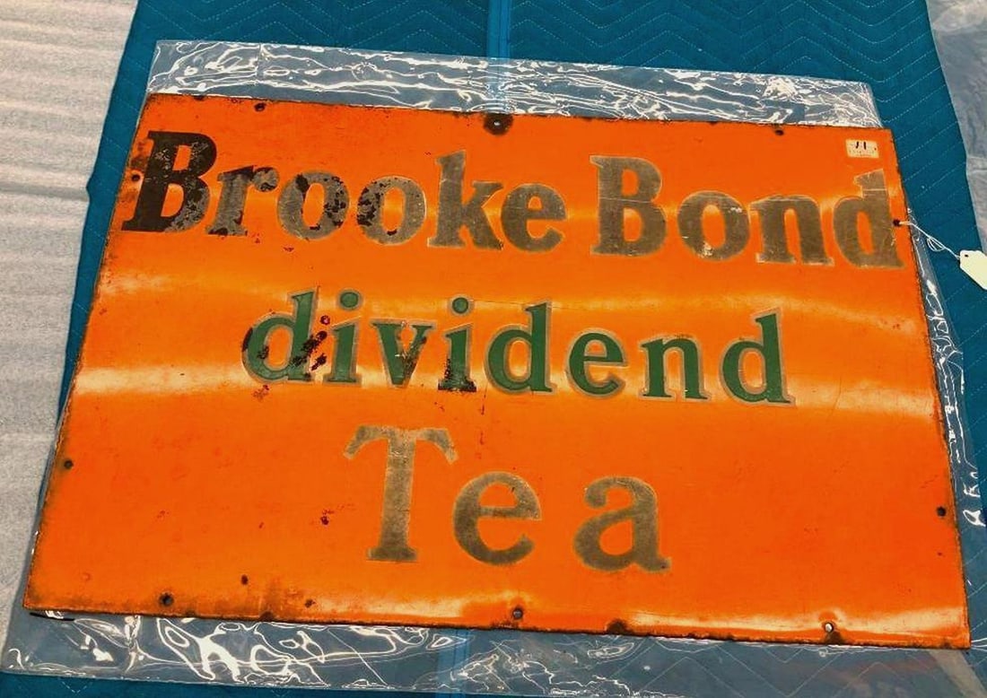 English Brooke Bond Dividend Tea Enameled Metal Sign: Circa 1930, the orange enameled metal rectangular sign with black lettering. Dimensions: 20" x 30" (50.8 x 76.2 cm) Overall fair condition. The sign is bowed. Some scratches enamel loss and rus/corros