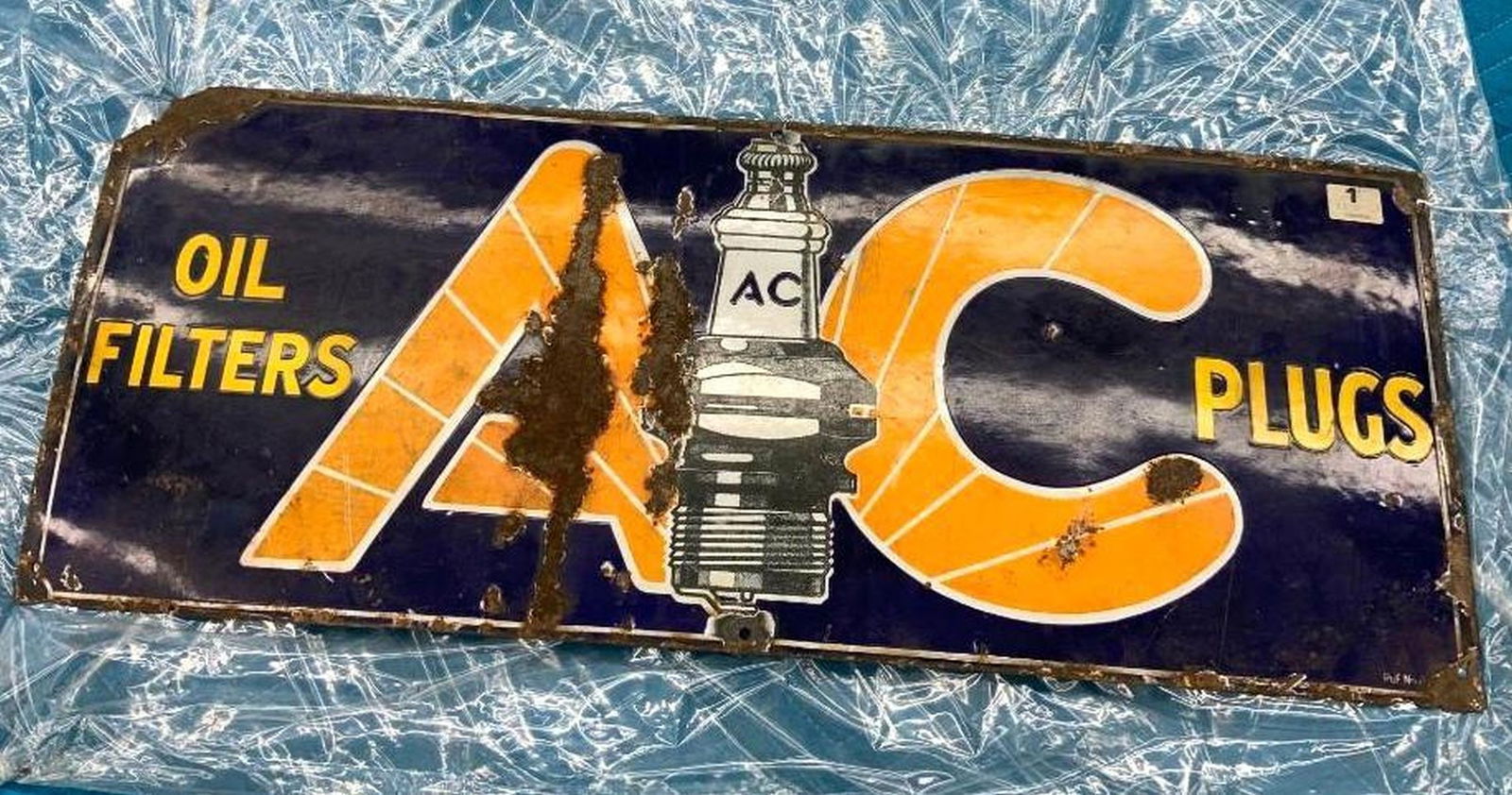 AC Plugs Advertising Sign: enameled metal sign. Date: c. 1930; Medium: metal, enamel; Dimensions: 12 x 30 inches (30.5 x 76.2 cm) Overall fair condition, Some enamel loss and rust to the front and corrosion allover to back. The