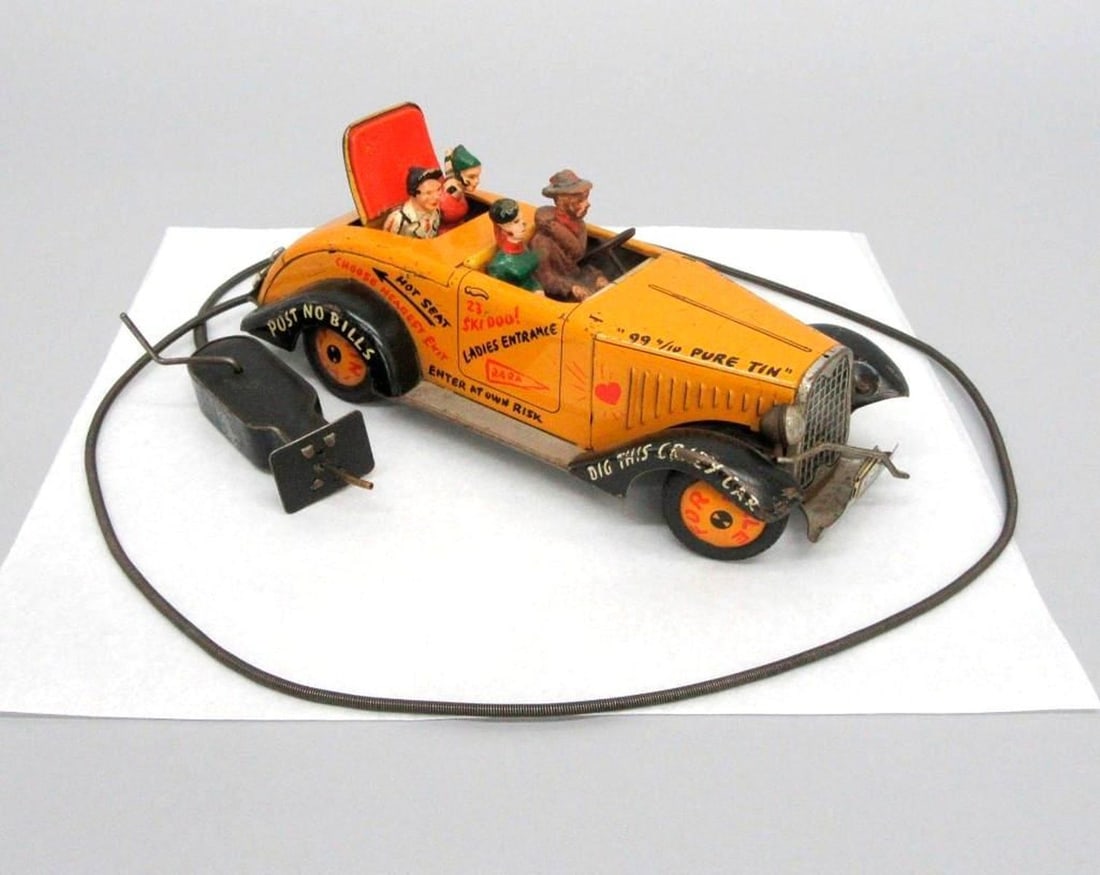 German Arnold Tin Lizzie Remote Car: A vintage lithographed tinplate toy car with attached remote; having a yellow exterior and with four figures in seats; a simple remote attached with cable. Dimensions: 4" x 3.75" x 9.5" (10.2 x 9.5 x