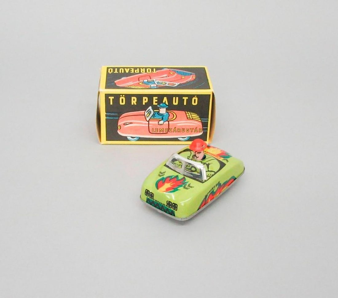 Hungarian Tin Liton Friction Torpeauto Car: Tinplate toy car; friction-powered; lime-green exterior with flame decals; driver's head is wearing bright red hat. .02: Original cardboard box; "Torpeauto / Lemezarugyad" printed on box; label
