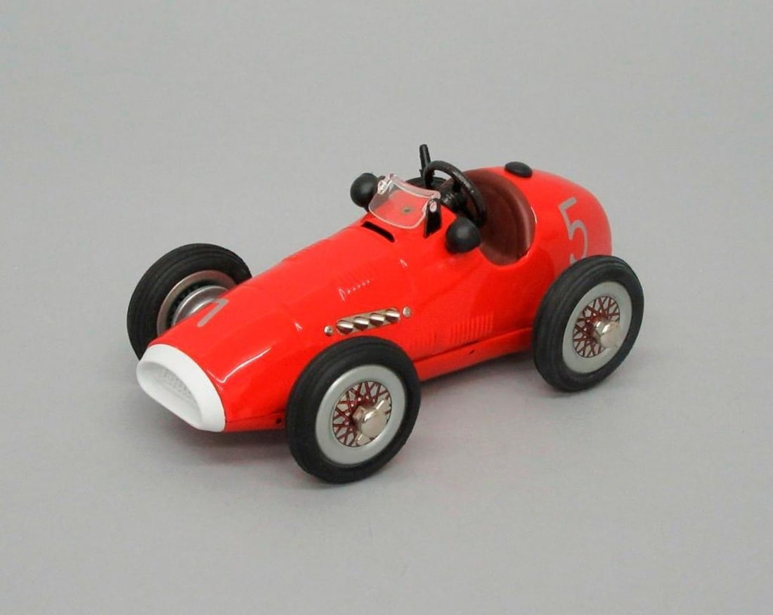 Schuco, Spuelwarenwerke Schreuer & Co. Grand Prix Racer Car: Bright red Grand Prix Racer toy car with black wheels and black steering wheel; silver-colored "5" painted on sides near front. Dimensions: 2.5" x 3.25" x 6.25" {good condition} SFO Museum