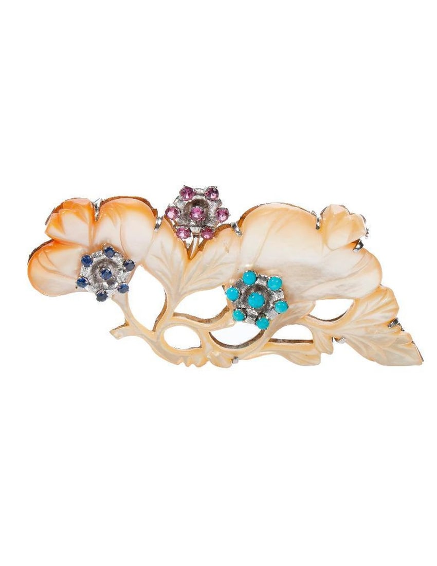 A gem-set and white metal brooch: designed with carved mother-of-pearl, accented by turquoise cabochons, a round sapphire, and red stones, mounted in white metal; measuring 3 7/8 x 1 /7/8 in.