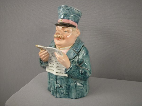 Majolica full figure humidor of man reading newspa: Majolica full figure humidor of man reading newspaper with blue hat and coat, 8 1/2", repair to corner of newspaper and hairline to base