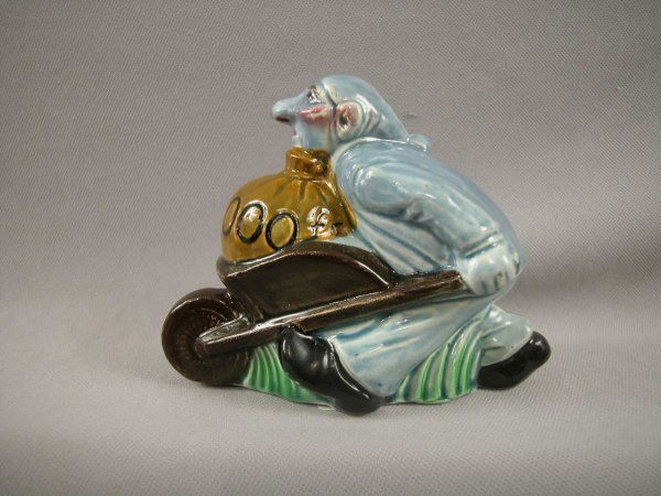 SARREGUEMINES figural ceramic bank in the form of: SARREGUEMINES figural ceramic bank in the form of a man pushing a wheel barrow full of a sack of money, 4 1/2", professional repair to money slot